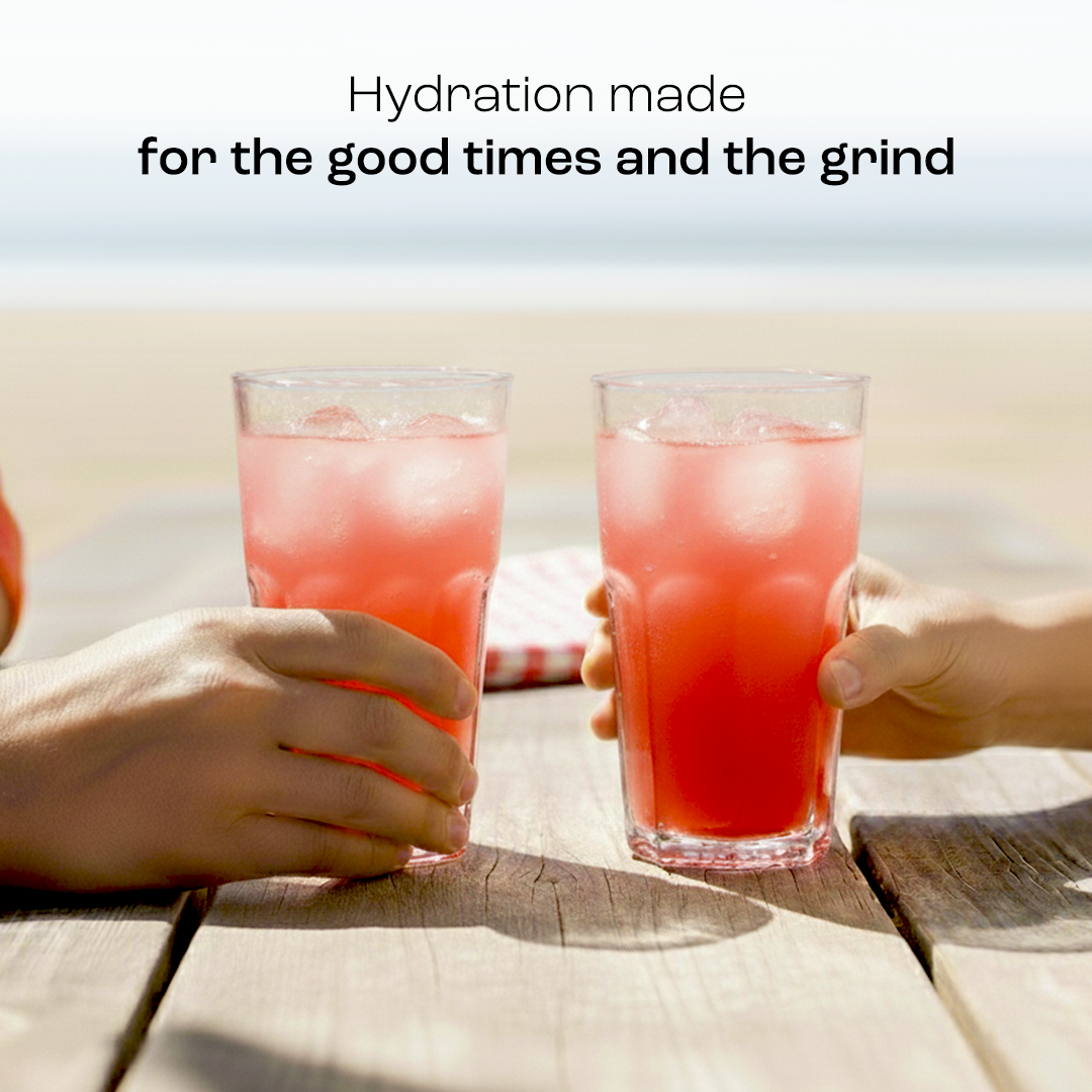 Two hands holding tall glasses of pink electrolyte drink with ice and bubbles