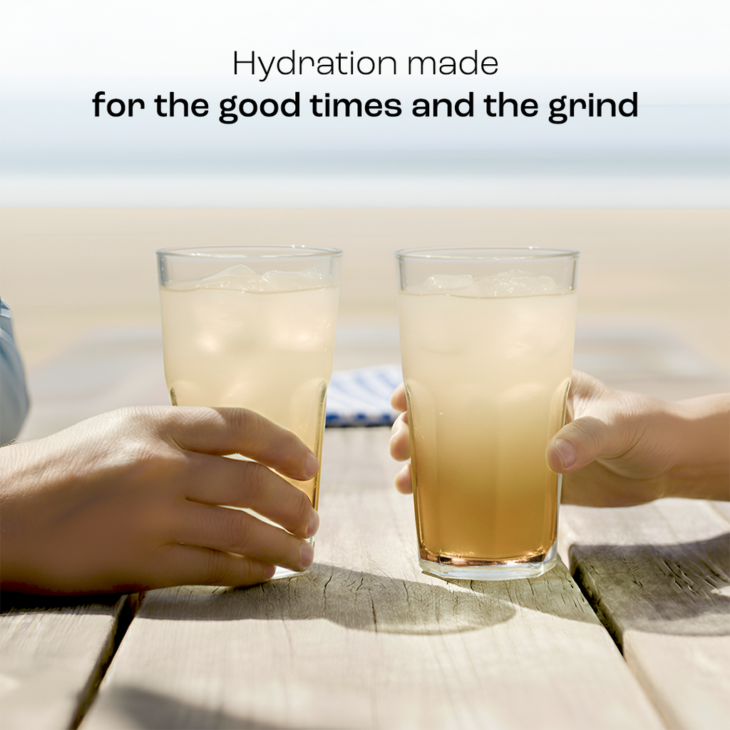 Two glasses of pale yellow electrolyte drink being held over a wooden surface