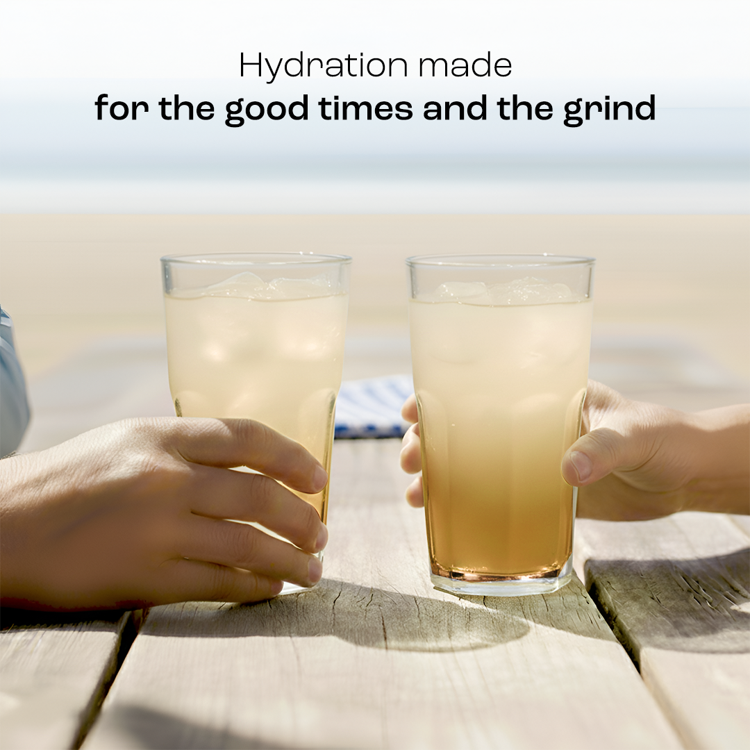 Two glasses of pale yellow electrolyte drink being held over a wooden surface