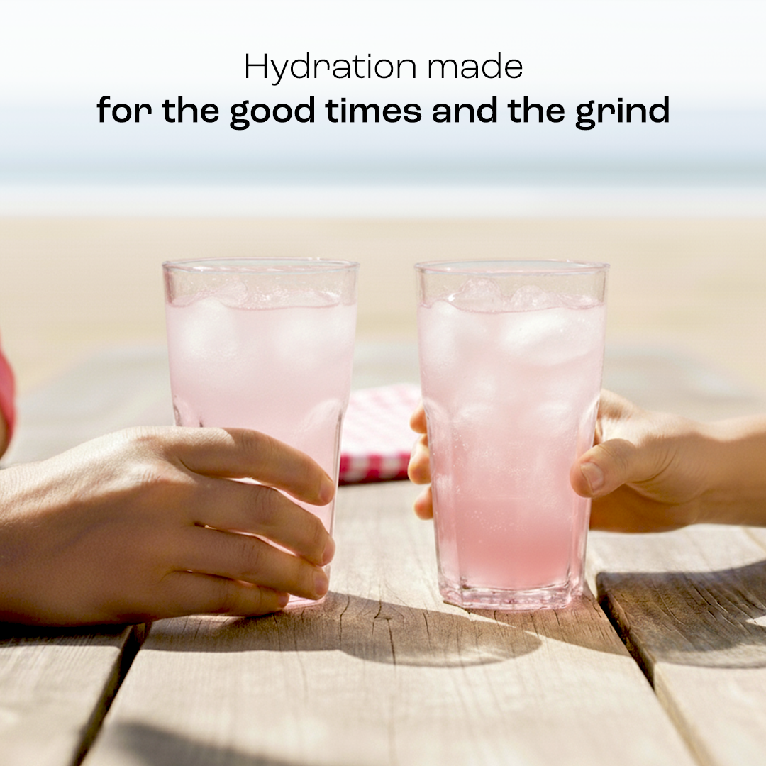 Two glasses of pink electrolyte drink clinking together in hands