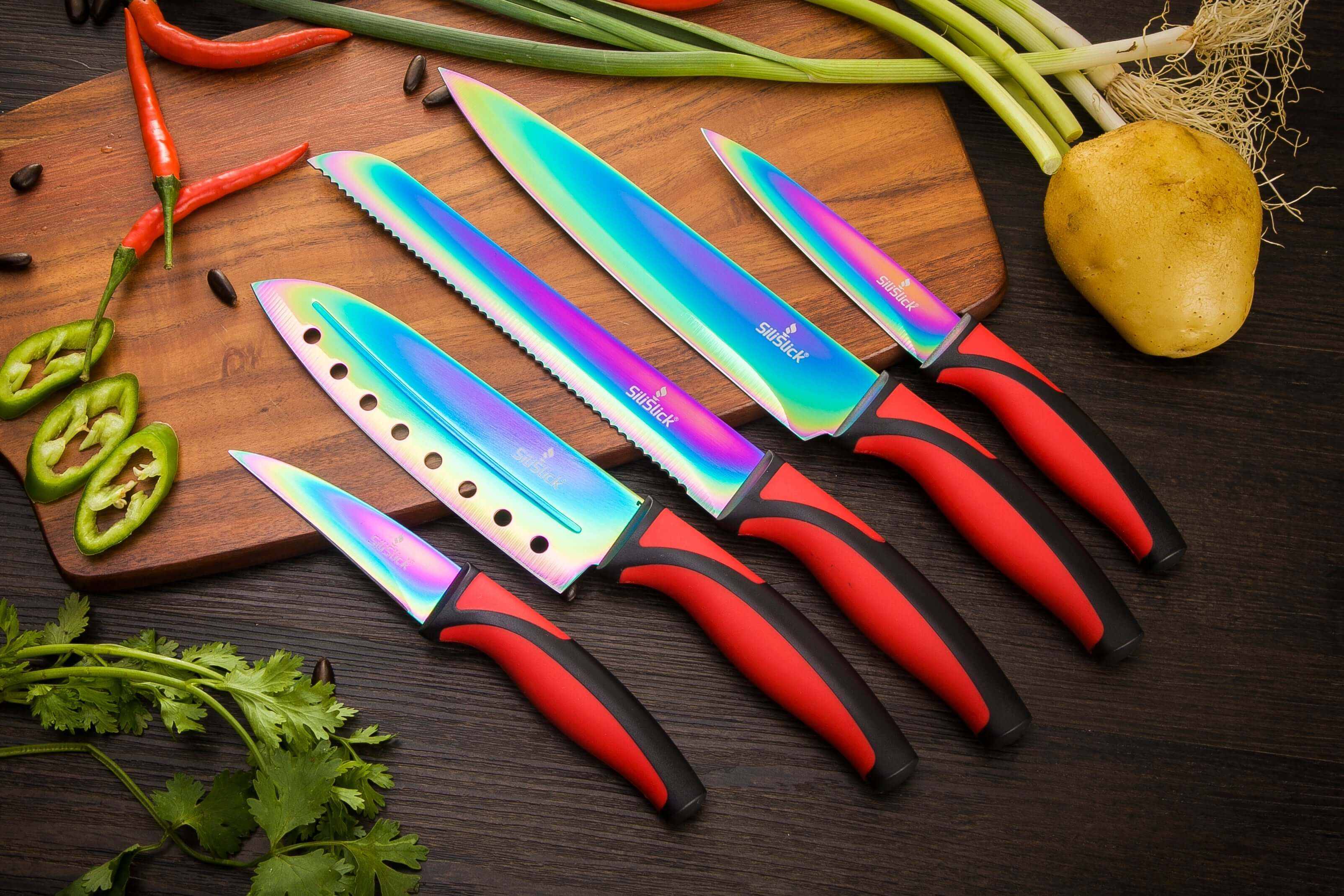 Knife set with red handles and rainbow blades, assorted sizes on cutting board