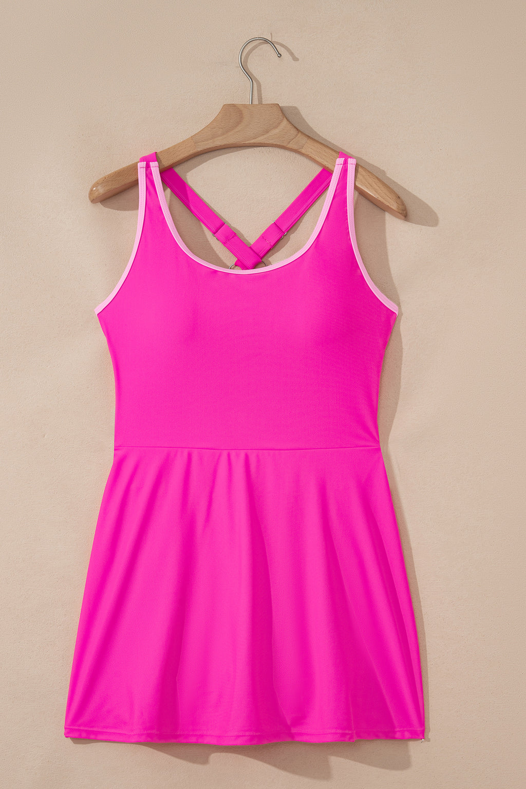 Bright pink swim dress with attached shorts, open back and contrast straps on hanger