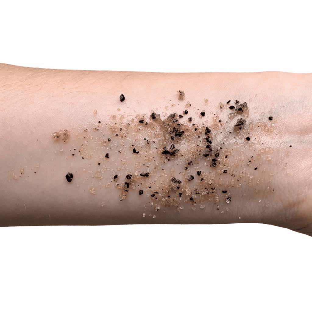 Exfoliating scrub on forearm skin with dark granules and sugar particles