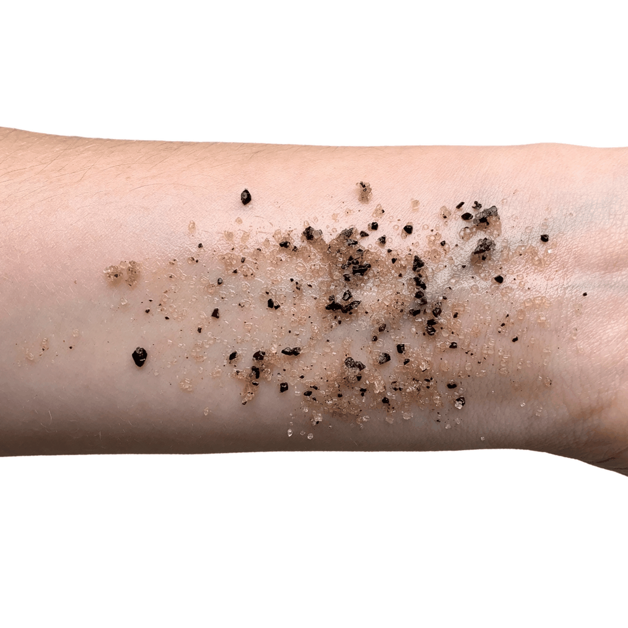 Exfoliating scrub on forearm skin with dark granules and sugar particles