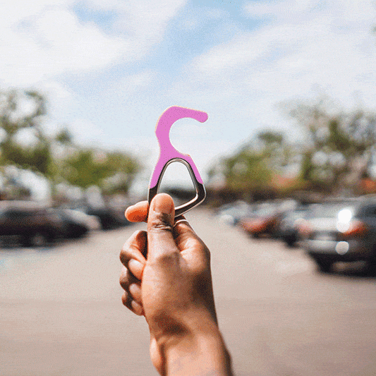 Pink silicone no-touch keychain tool with metal ring, held on a path